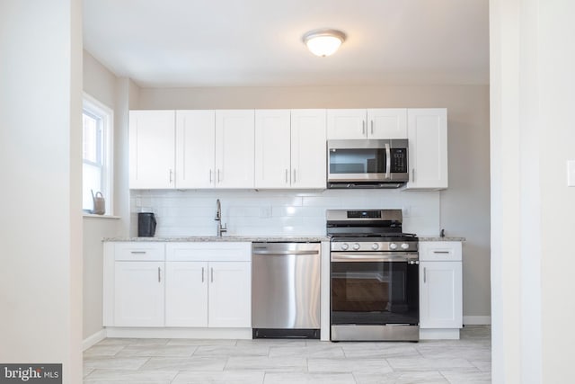 kitchen featuring tasteful backsplash, white cabinetry, appliances with stainless steel finishes, and light stone counters