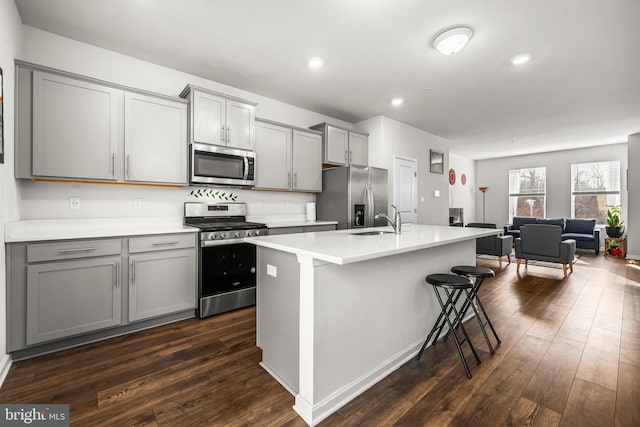 kitchen featuring sink, appliances with stainless steel finishes, gray cabinetry, an island with sink, and dark hardwood / wood-style flooring