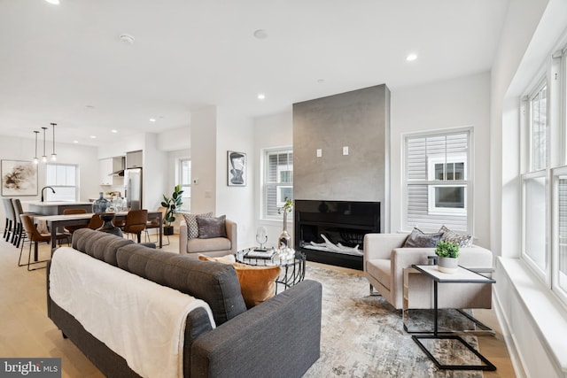 living room with sink, a wealth of natural light, a large fireplace, and light wood-type flooring