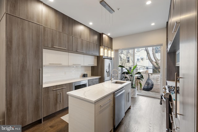 kitchen with appliances with stainless steel finishes, dark hardwood / wood-style floors, decorative light fixtures, sink, and a center island with sink