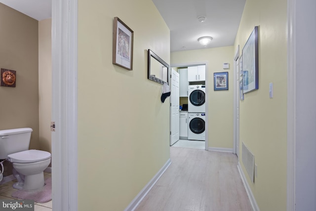 hall with stacked washing maching and dryer and light hardwood / wood-style flooring