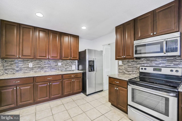 kitchen featuring stainless steel appliances, light stone counters, light tile patterned flooring, and decorative backsplash