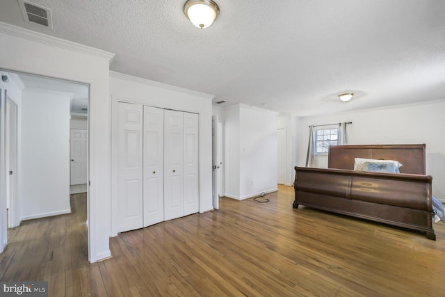 unfurnished bedroom with a closet, visible vents, ornamental molding, a textured ceiling, and wood finished floors