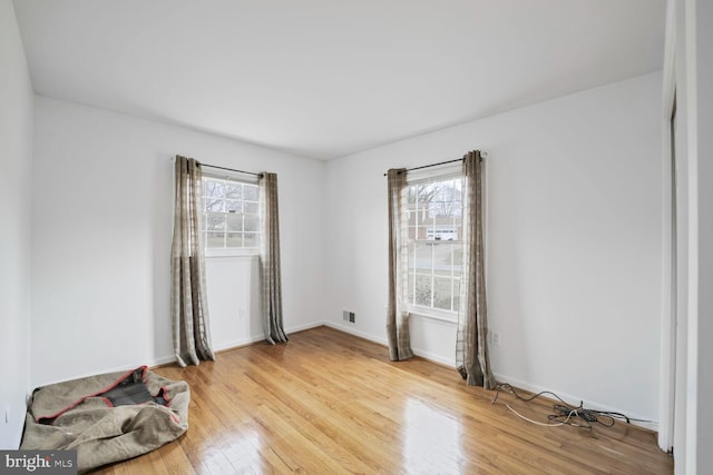 unfurnished room featuring plenty of natural light, light wood-type flooring, visible vents, and baseboards