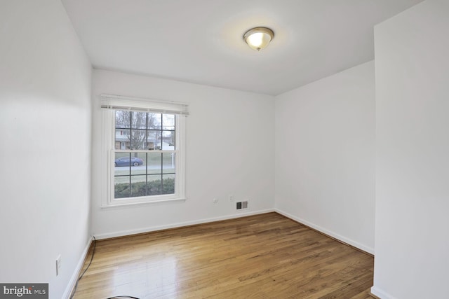 unfurnished room featuring wood finished floors, visible vents, and baseboards