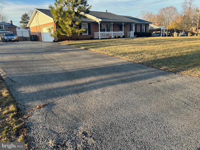 view of front of home with brick siding, a porch, a garage, driveway, and a front lawn