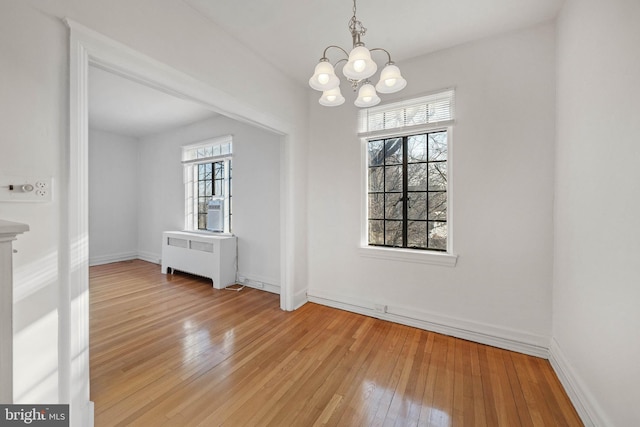 unfurnished dining area featuring a notable chandelier, radiator heating unit, and light wood-type flooring