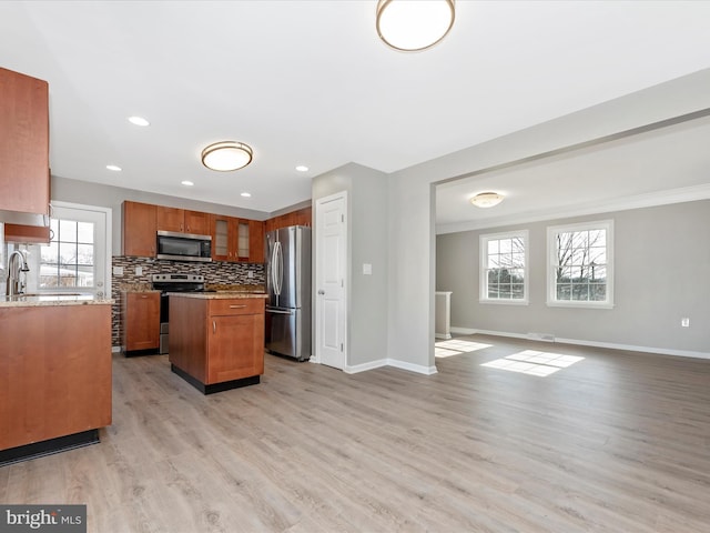 kitchen with a kitchen island, tasteful backsplash, light stone counters, stainless steel appliances, and light wood-type flooring