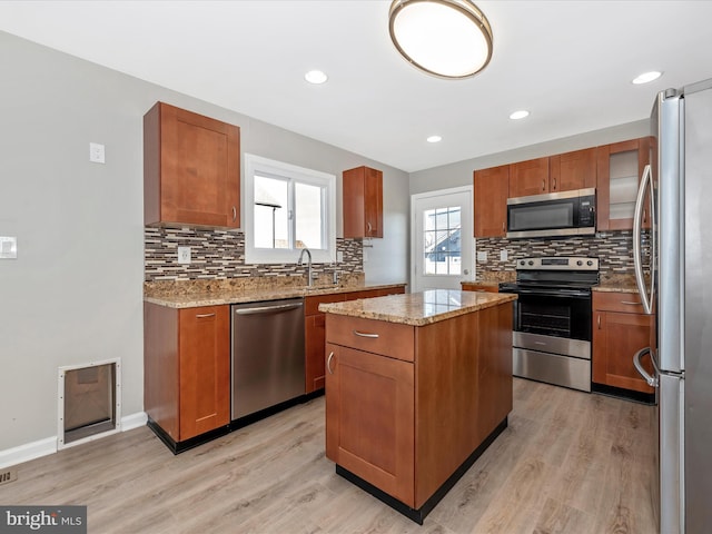 kitchen featuring a kitchen island, decorative backsplash, light hardwood / wood-style floors, stainless steel appliances, and light stone countertops