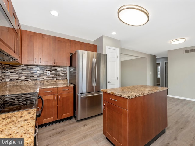 kitchen with range with electric stovetop, tasteful backsplash, stainless steel fridge, light stone counters, and light wood-type flooring