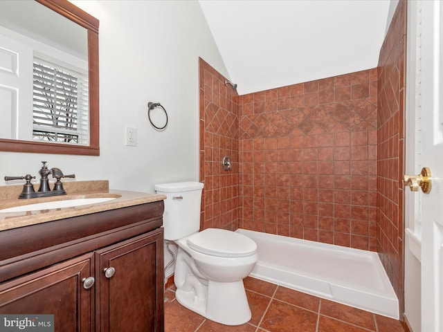 bathroom featuring a tile shower, vanity, vaulted ceiling, tile patterned floors, and toilet