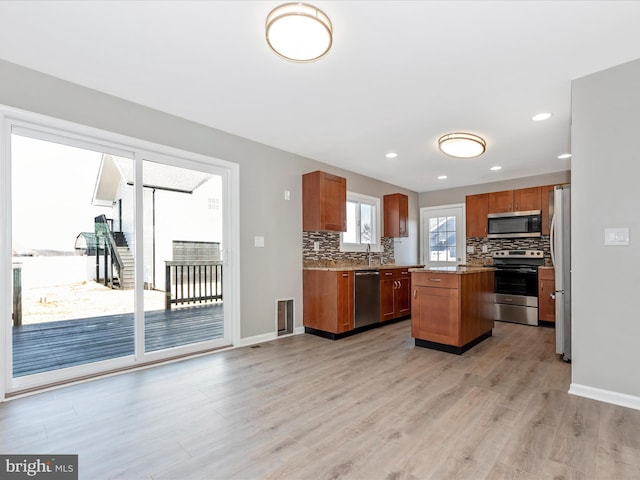 kitchen with appliances with stainless steel finishes, decorative backsplash, a center island, light stone counters, and light hardwood / wood-style flooring