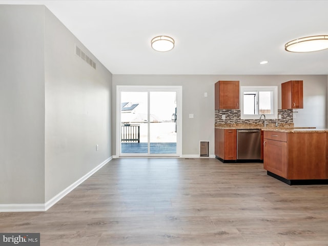 kitchen featuring sink, decorative backsplash, stainless steel dishwasher, light stone countertops, and light wood-type flooring