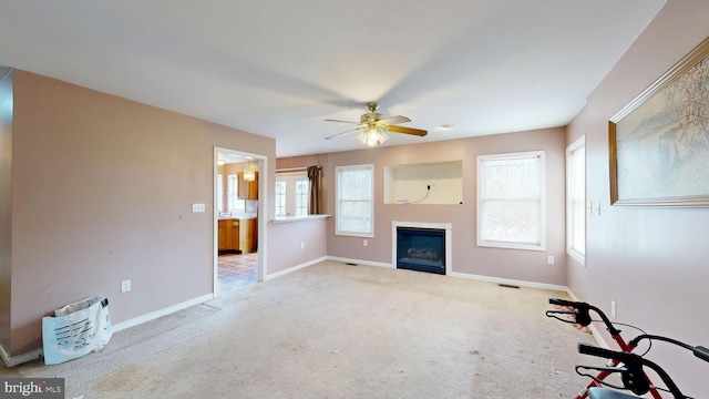 unfurnished living room with ceiling fan, baseboards, carpet flooring, and a glass covered fireplace