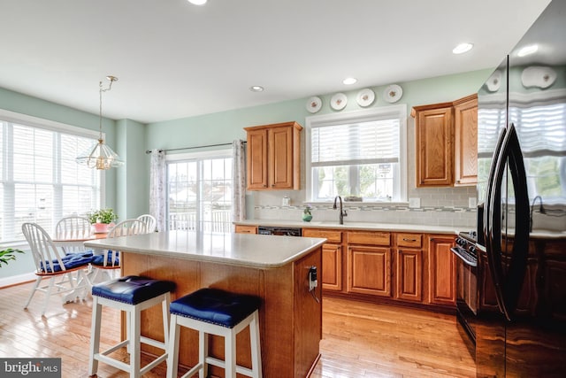 kitchen with pendant lighting, decorative backsplash, a center island, light hardwood / wood-style floors, and black appliances