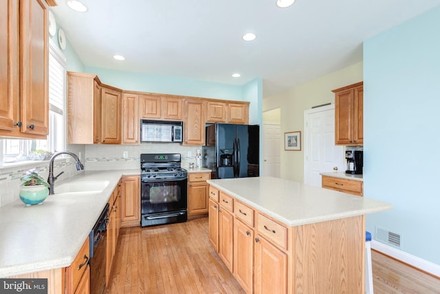 kitchen featuring sink, backsplash, black appliances, light hardwood / wood-style floors, and a kitchen island