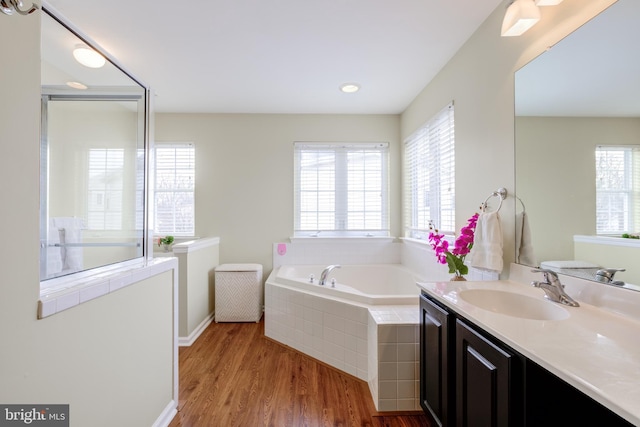 bathroom featuring vanity, a relaxing tiled tub, and wood-type flooring