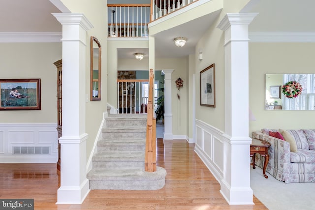 entrance foyer with decorative columns, crown molding, and light wood-type flooring