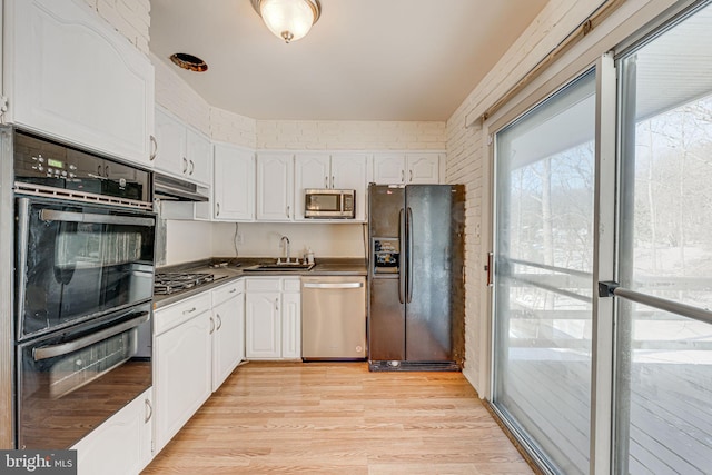 kitchen featuring sink, black appliances, light wood-type flooring, brick wall, and white cabinets