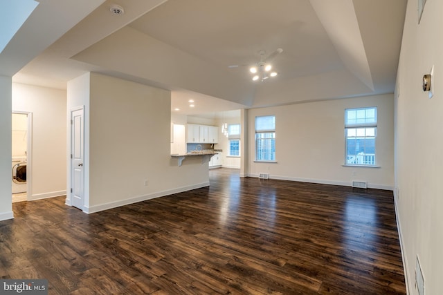 unfurnished living room featuring a healthy amount of sunlight, washer / clothes dryer, dark hardwood / wood-style flooring, and a raised ceiling