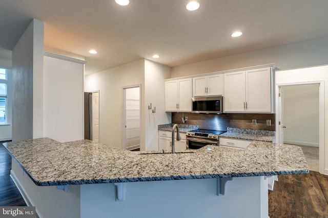 kitchen with a breakfast bar, white cabinetry, stainless steel appliances, a spacious island, and dark hardwood / wood-style flooring