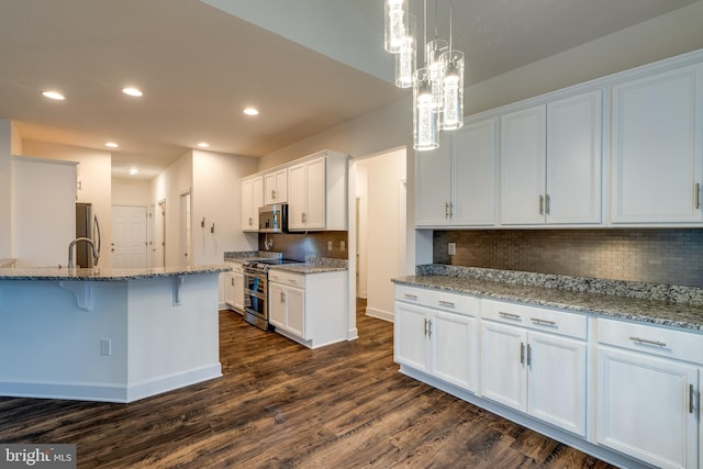 kitchen with stainless steel appliances, white cabinetry, light stone countertops, and a kitchen breakfast bar