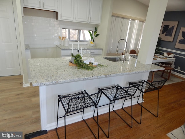 kitchen with a breakfast bar, white cabinetry, sink, light stone countertops, and light wood-type flooring