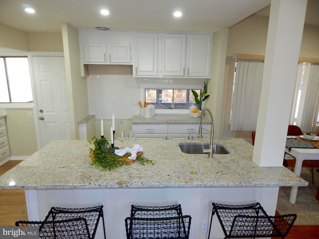 kitchen with light stone counters, sink, tasteful backsplash, and white cabinets