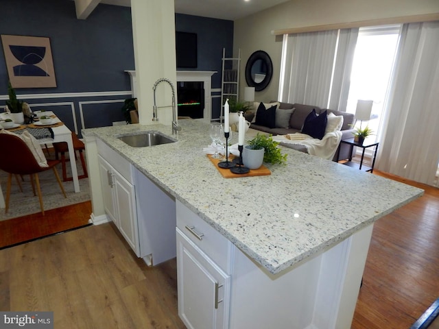 kitchen with light wood-type flooring, light stone countertops, sink, and white cabinets