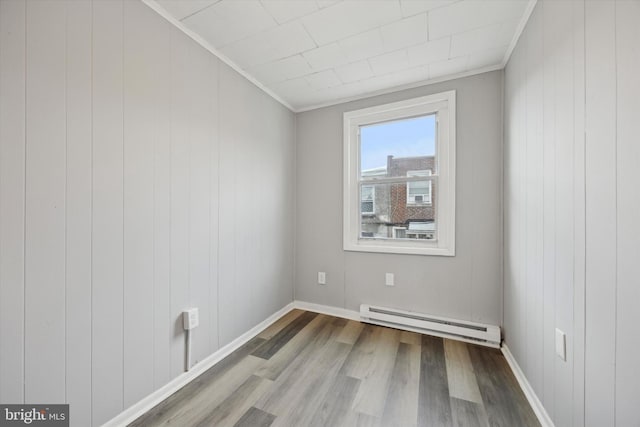 spare room with hardwood / wood-style floors, crown molding, and a baseboard radiator