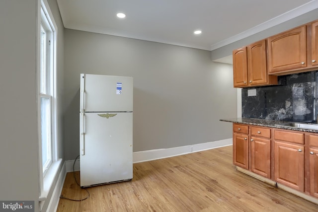 kitchen featuring sink, light hardwood / wood-style flooring, white refrigerator, dark stone counters, and backsplash