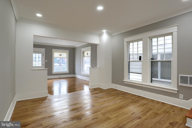 empty room featuring crown molding, a wealth of natural light, and light wood-type flooring