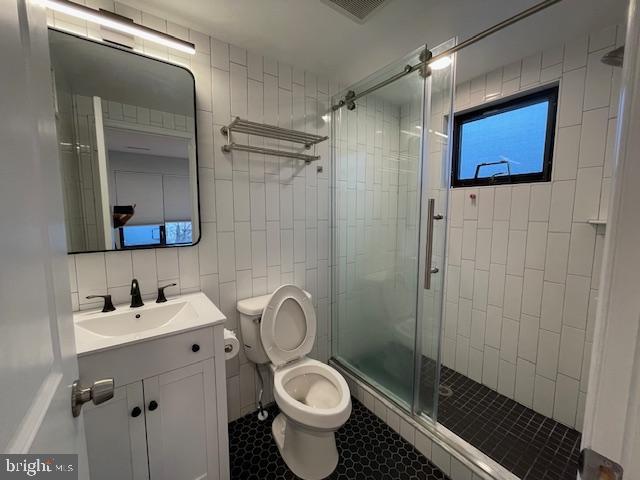 bathroom with toilet, tile walls, vanity, walk in shower, and decorative backsplash