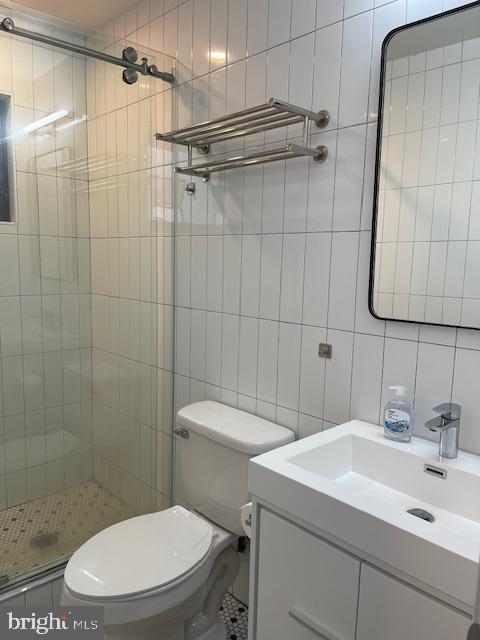 bathroom with toilet, tiled shower, tile walls, and vanity