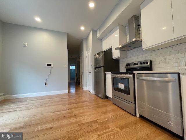 kitchen featuring white cabinets, stainless steel appliances, wall chimney range hood, and tasteful backsplash