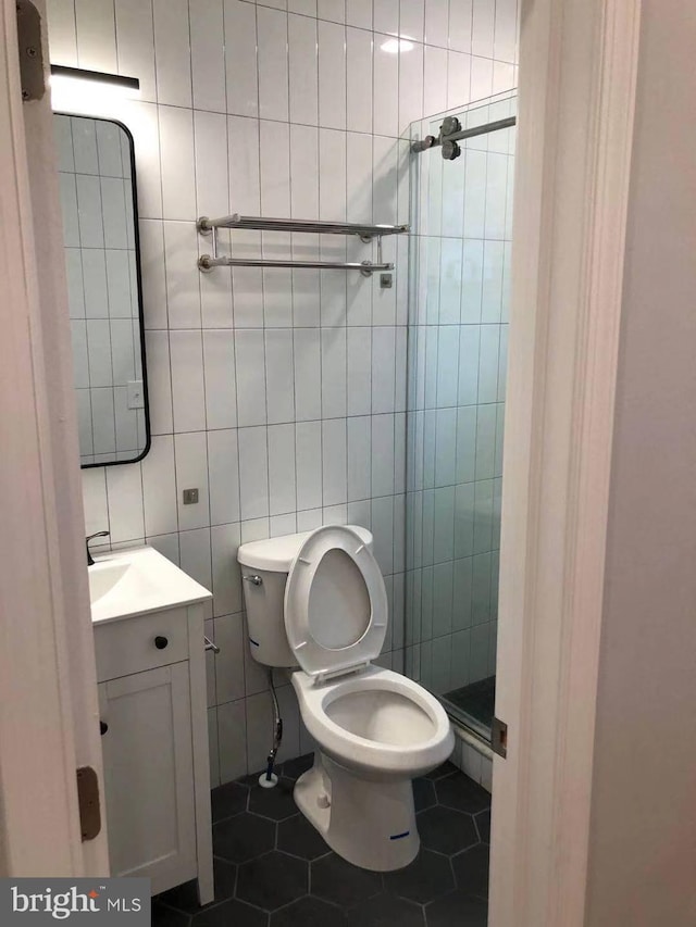 bathroom featuring tile patterned floors, toilet, tile walls, vanity, and tiled shower