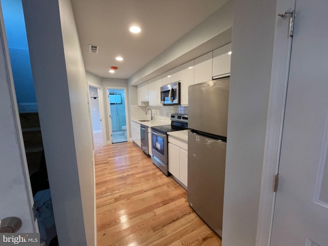 kitchen featuring light wood-type flooring, stainless steel appliances, decorative backsplash, sink, and white cabinetry