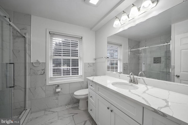 bathroom with vanity, toilet, a shower with shower door, and tile walls