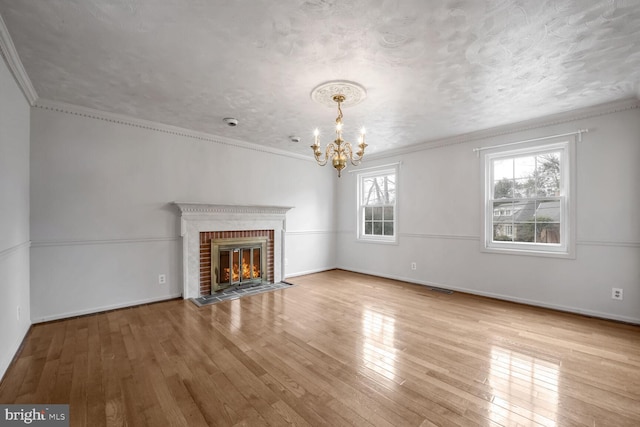 unfurnished living room with ornamental molding, a brick fireplace, a textured ceiling, an inviting chandelier, and light hardwood / wood-style flooring