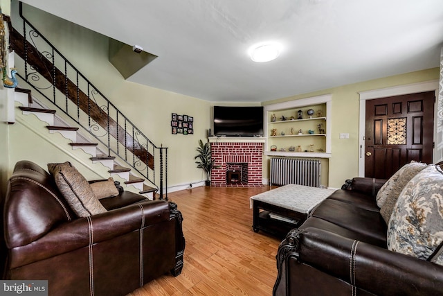 living room featuring hardwood / wood-style floors, radiator heating unit, and a brick fireplace