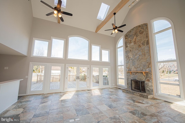 unfurnished living room with ceiling fan, a fireplace, a skylight, and a high ceiling