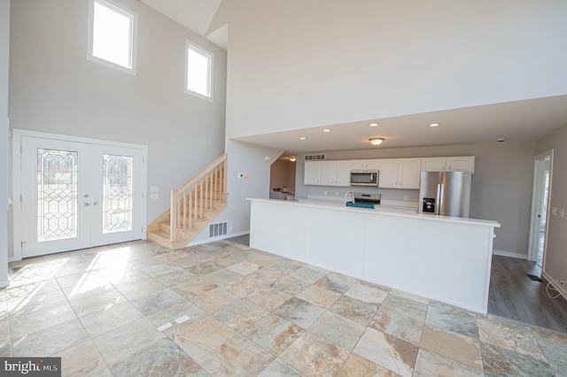 interior space featuring a towering ceiling, white cabinetry, sink, stainless steel appliances, and french doors