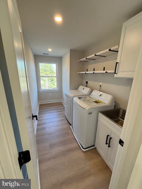 washroom with cabinets, sink, washing machine and clothes dryer, and light hardwood / wood-style flooring