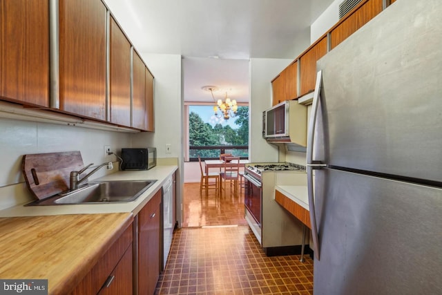 kitchen with stainless steel appliances, sink, pendant lighting, and an inviting chandelier