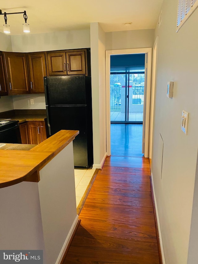 kitchen featuring black refrigerator, hardwood / wood-style flooring, wood counters, and a kitchen bar