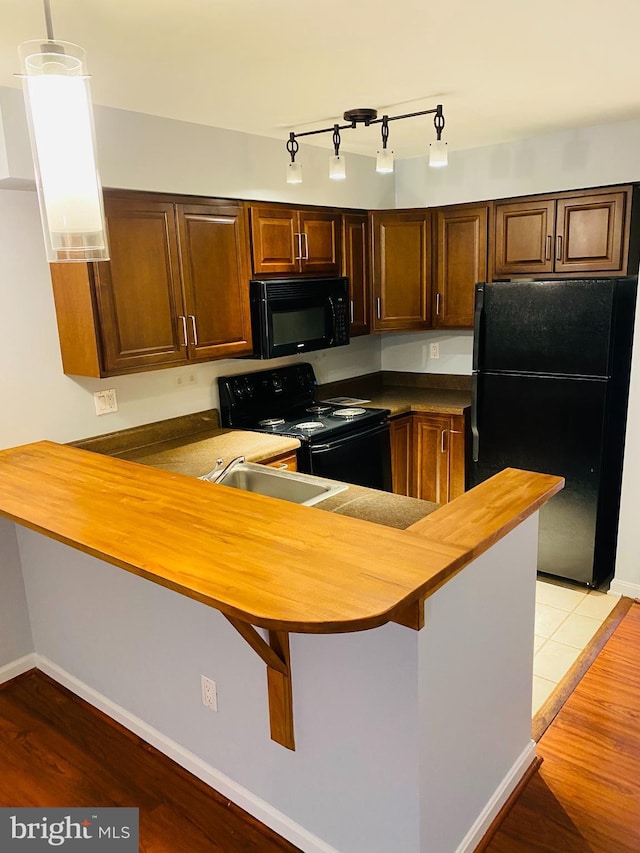 kitchen with decorative light fixtures, kitchen peninsula, light hardwood / wood-style flooring, and black appliances