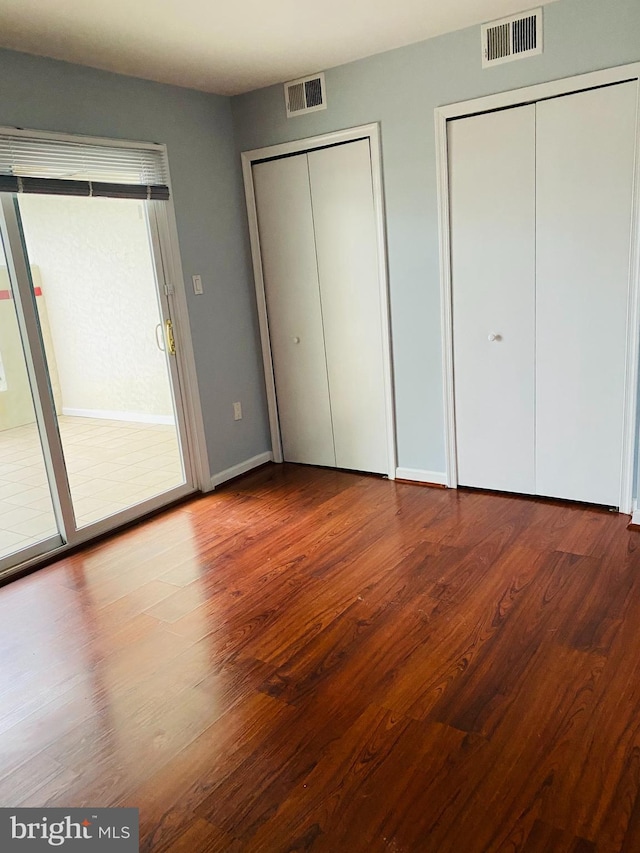 unfurnished bedroom featuring hardwood / wood-style floors and multiple closets