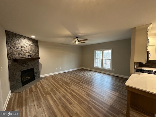 unfurnished living room featuring dark hardwood / wood-style flooring, a stone fireplace, and ceiling fan