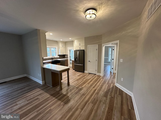 kitchen featuring a kitchen breakfast bar, dark hardwood / wood-style flooring, black fridge with ice dispenser, and white cabinets