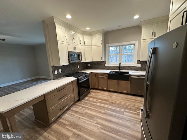 kitchen with sink, light hardwood / wood-style flooring, appliances with stainless steel finishes, decorative backsplash, and white cabinets